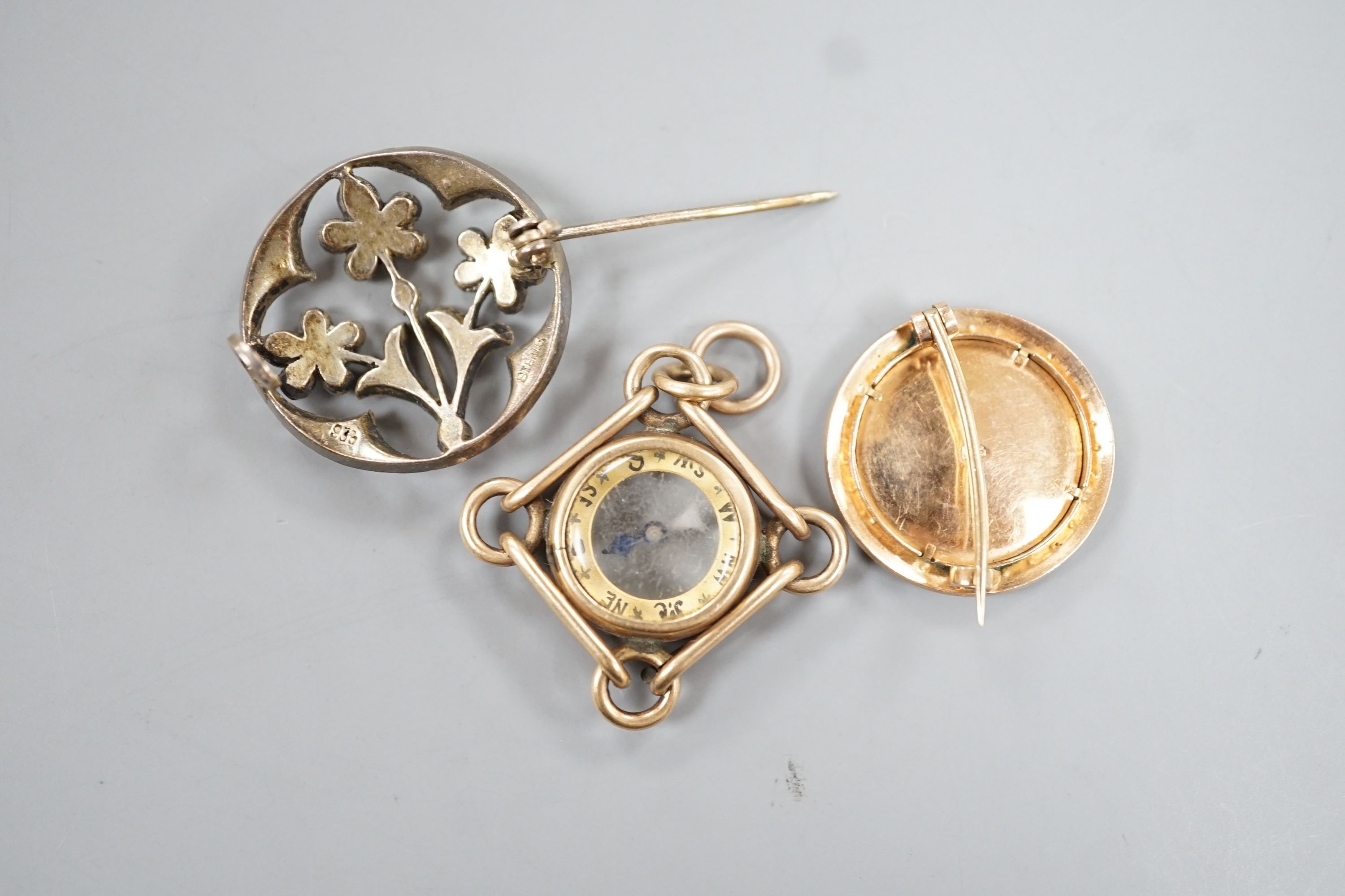 An American 10k yellow metal compass pendant, 29mm, gross 7.1 grams, a 585 and split pearl set circular portrait brooch, gross 4 grams and a two colour paste set brooch.